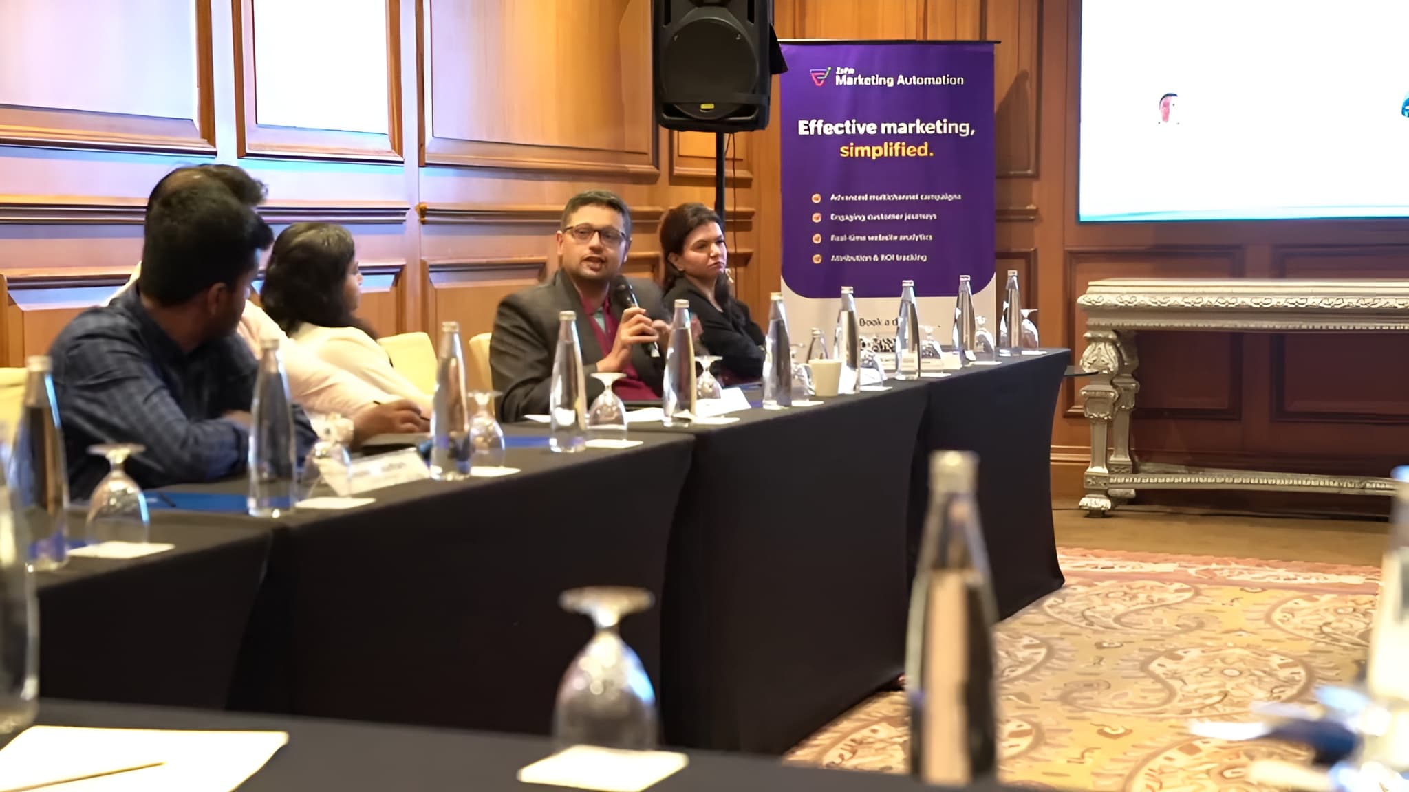 A panellist answering a question into a microphone, beside the Zoho Marketing Automation banner