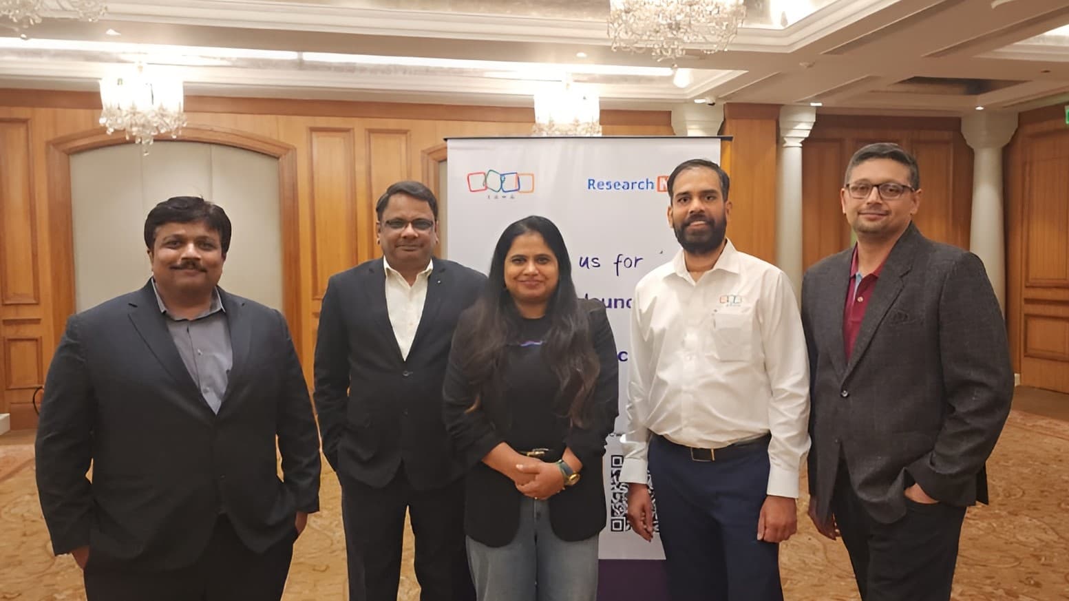 Five speakers standing together in front of the Zoho and Research NXT banner at Hilton Mumbai